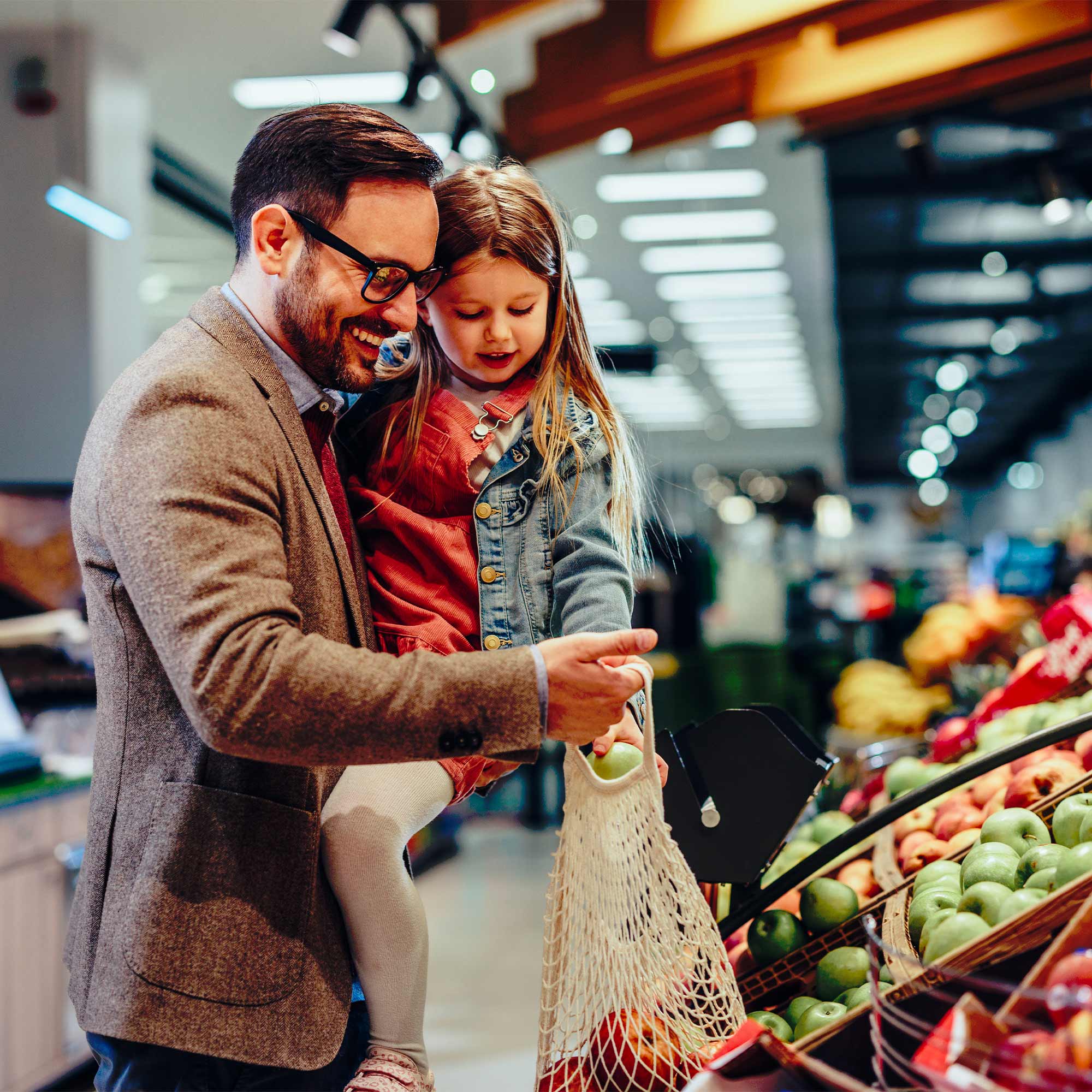 A father carries his young daughter as they grocery shop.